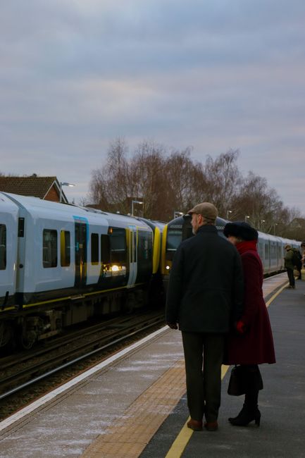 A quiet train platform at Pinner Station during early evening, with a polished concrete surface showing reflections of the overhead lighting. The platform features tactile paving strips near the edge 